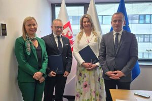 Podpisanie umowy na granty osiedlowe, osoby pozują do zdjęcia na tle flag