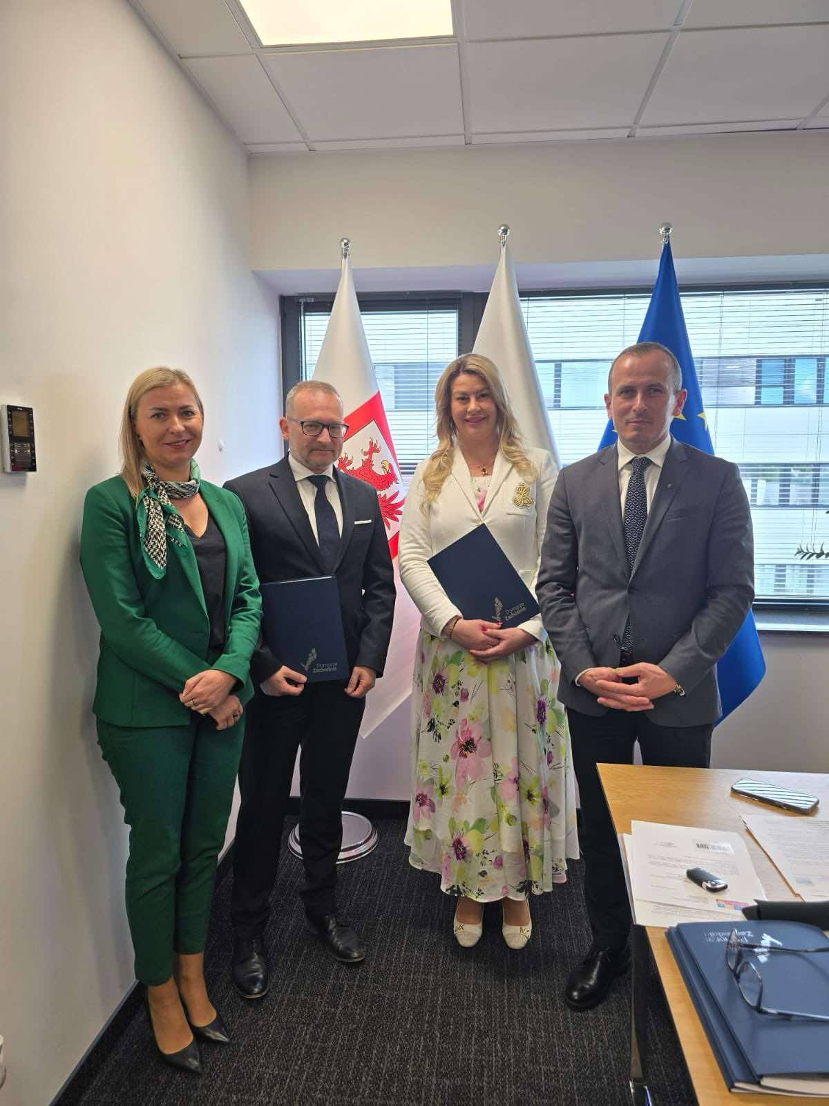 Podpisanie umowy na granty osiedlowe, osoby pozują do zdjęcia na tle flag